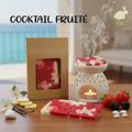 la photo présente une Tablette style puzzle de fondants blancs et rouges parfumés en cire d'olive naturelle, sans produits chimiques, vegan, emballée dans un étui couleur kraft avec fenêtre transparente pour voir le produit à l'intérieur. On voit également sur la photo des fraise, banane, mure, banane et  vanille et un brule parfum blanc duquel s'élèvent des effluves envoutantes